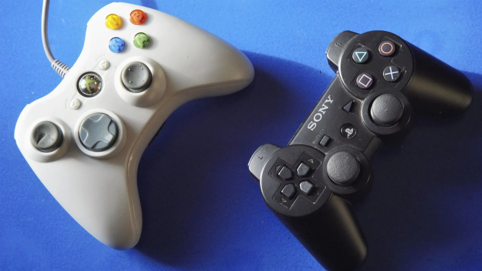 Hai tay cầm chơi game Xbox 360 và PlayStation 3 đặt trên bề mặt xanh, tượng trưng cho sự kết nối giữa các nền tảng chơi game nhờ cross-play.