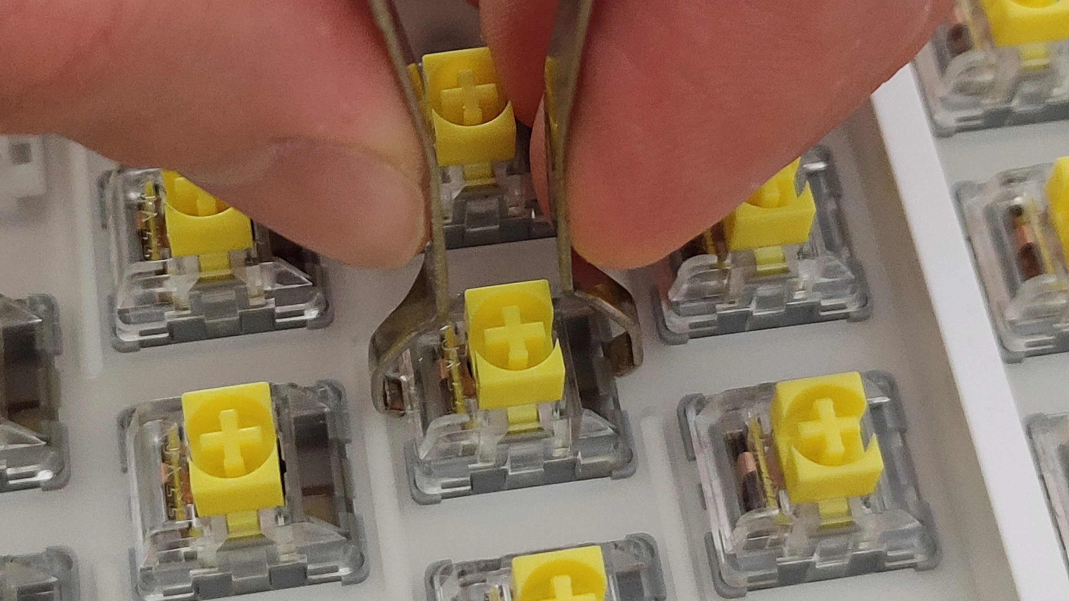 Hình ảnh bàn tay đang tháo switch bàn phím cơ bằng dụng cụ chuyên dụng, minh họa khả năng thay thế và sửa chữa dễ dàng