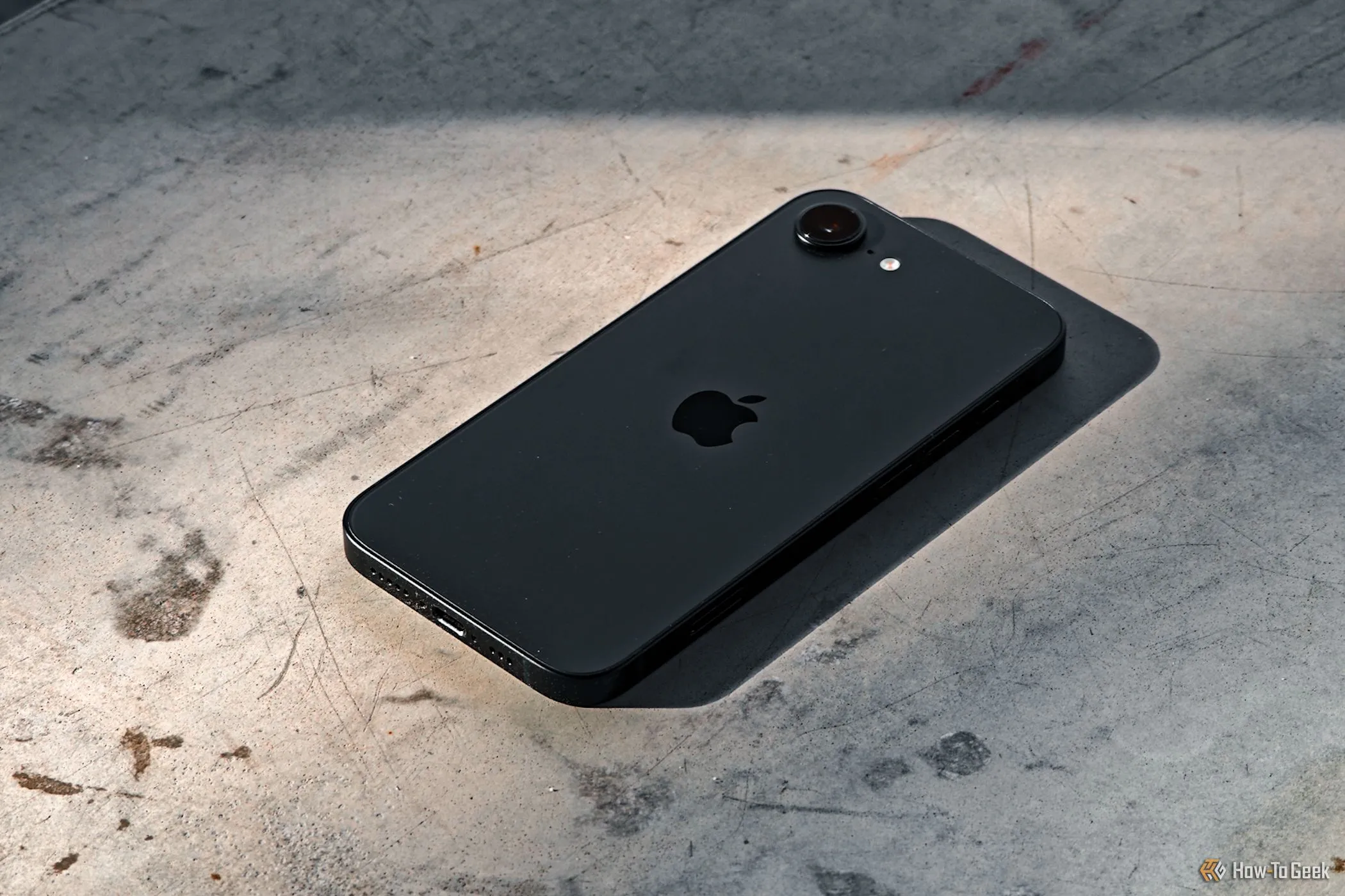 Mặt lưng của iPhone 16e úp trên nền bê tông, nổi bật cụm camera và chất liệu hoàn thiện.