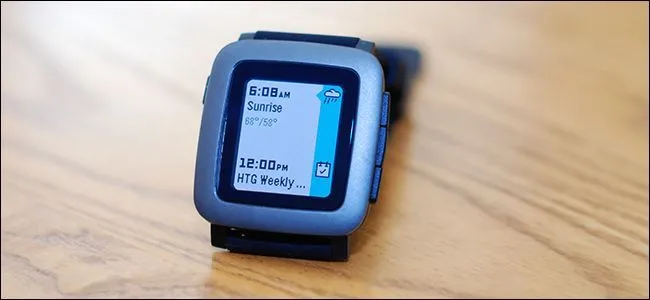Một chiếc đồng hồ Pebble màu đen với màn hình đơn sắc hiển thị giờ trên nền gỗ.