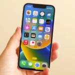 Một người phụ nữ đang cầm chiếc iPhone 13 Mini màu xanh lá cây, thể hiện kích thước nhỏ gọn dễ sử dụng bằng một tay.