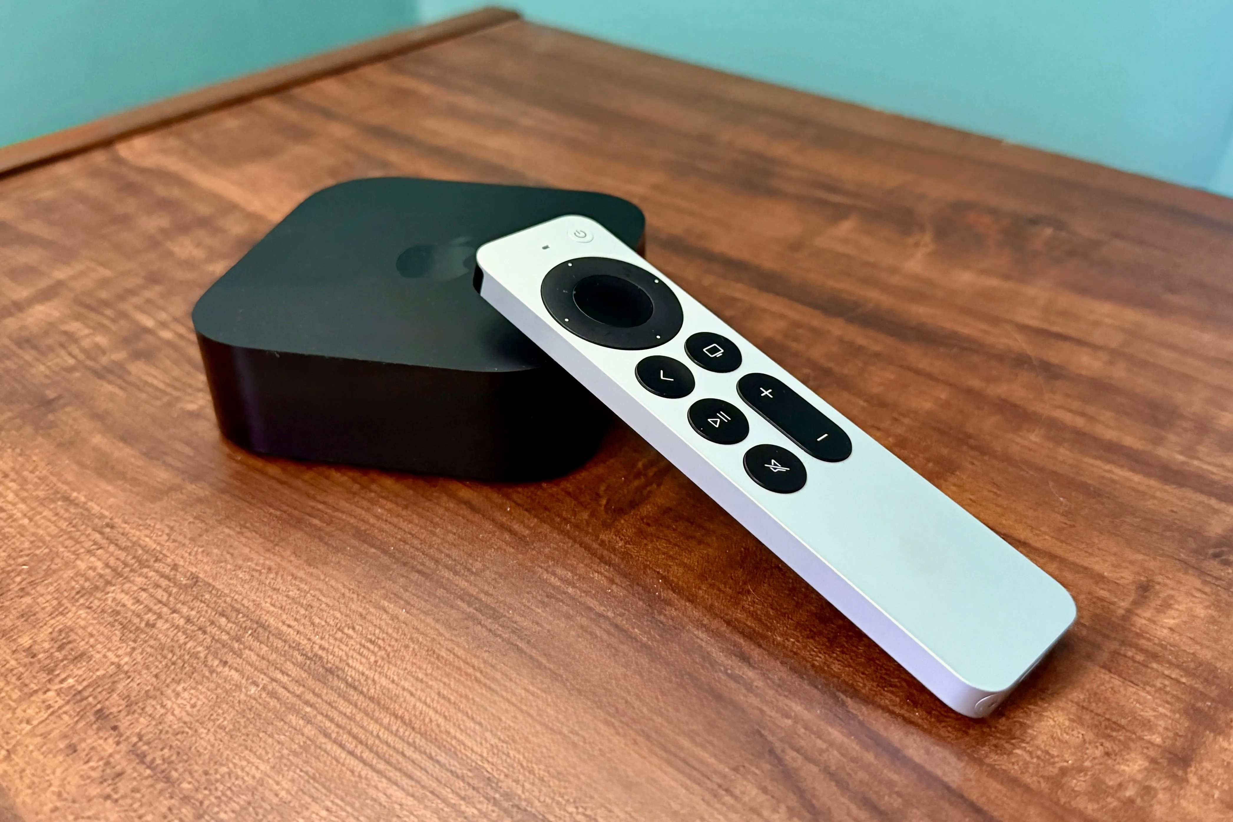 Thiết bị Apple TV 4K màu đen và điều khiển Siri Remote đặt trên bàn gỗ, thể hiện tính năng giải trí gia đình