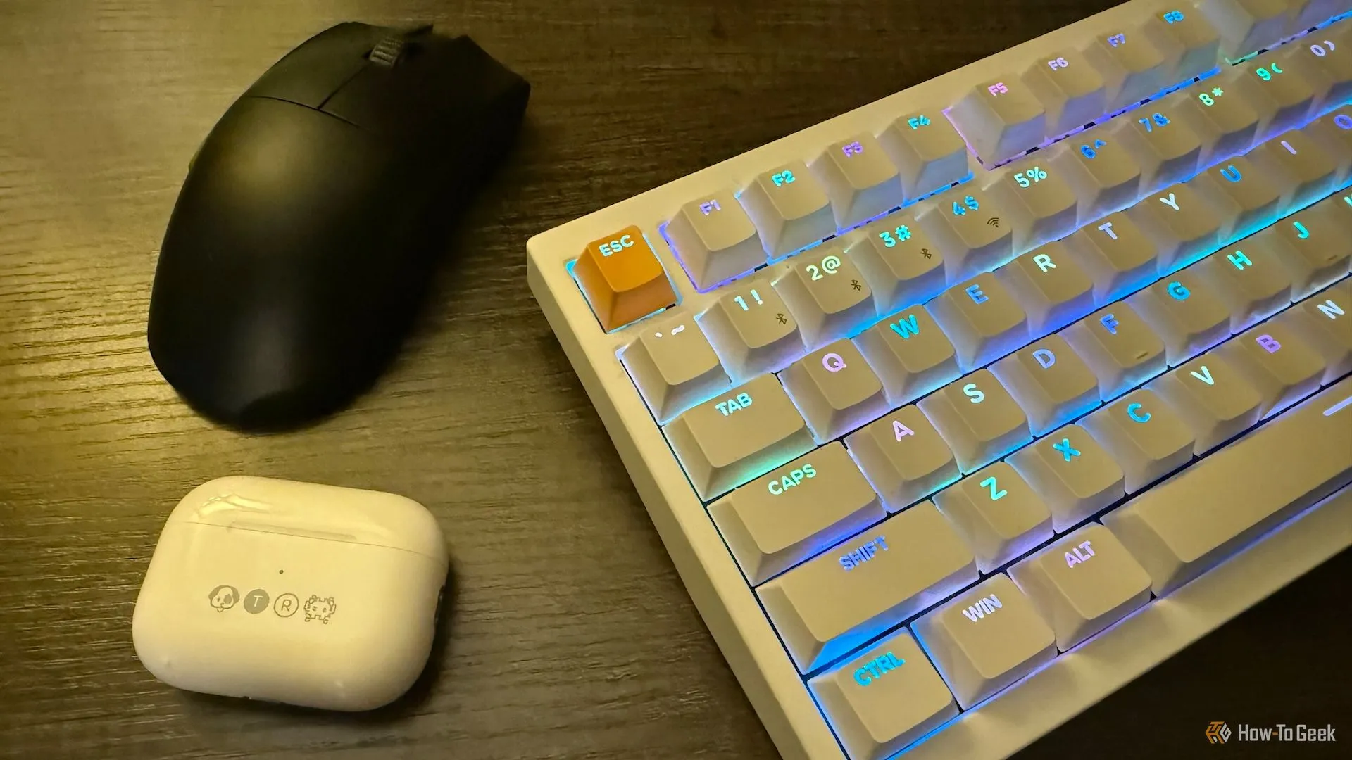 Apple AirPods Pro trong hộp khắc, chuột không dây Razer Viper V3 Pro và bàn phím từ tính không dây Keychron K2 HE trên bàn làm việc gọn gàng.