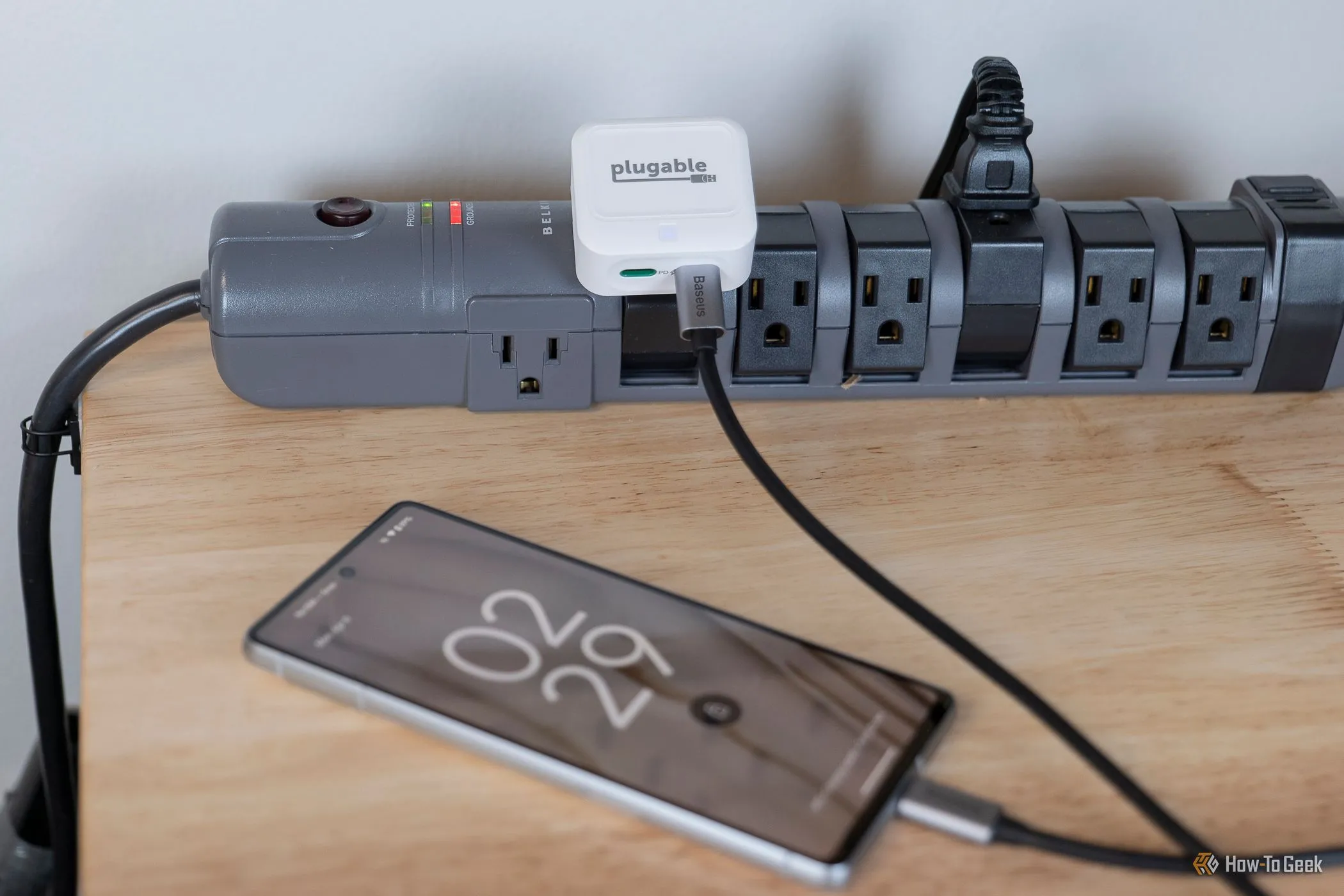 Bộ sạc Plugable 40W Dual USB-C đang sạc một chiếc điện thoại iPhone trên bàn, minh họa khả năng sạc nhanh và đồng thời cho thiết bị di động.