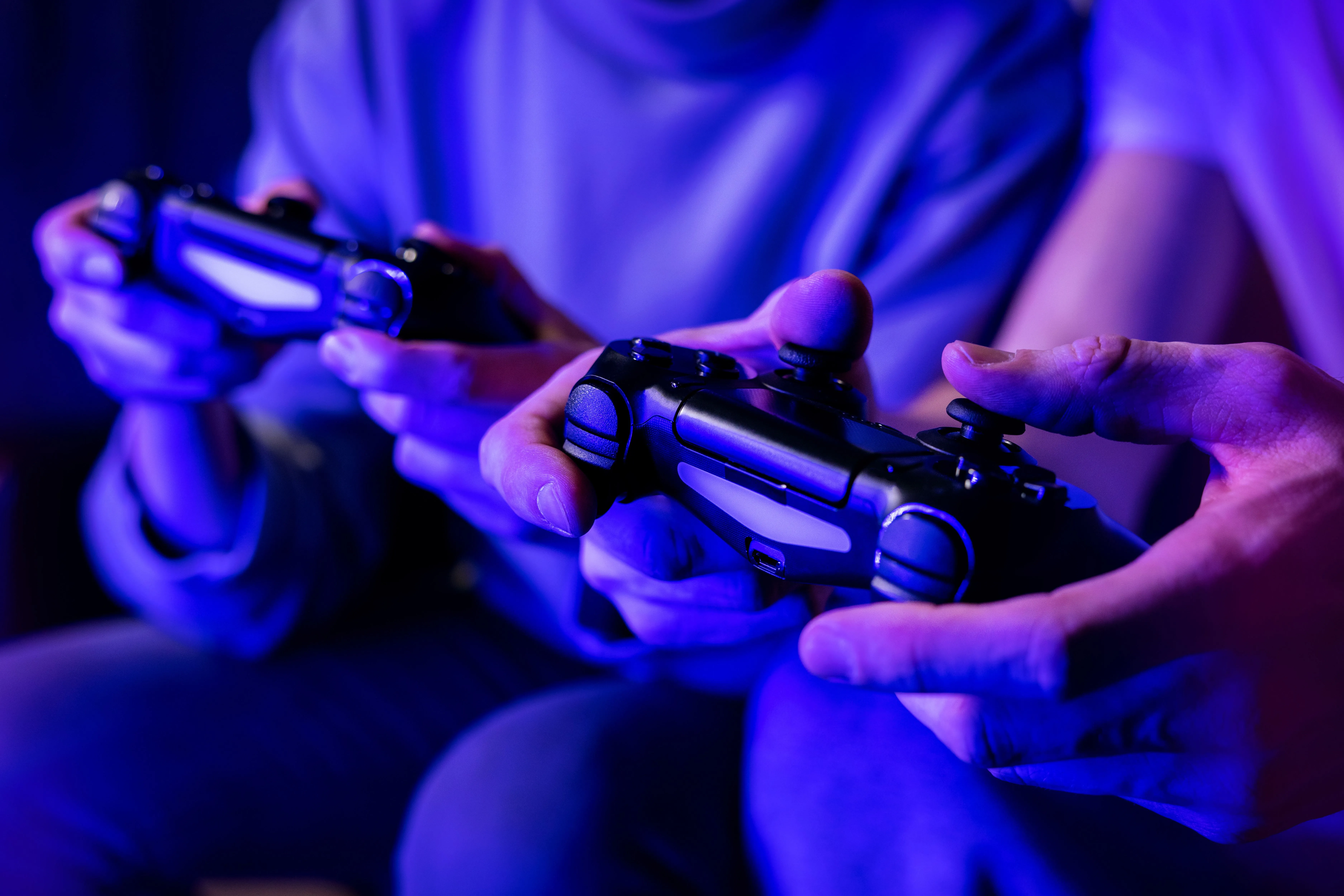Hai người bạn đang chơi game nhiều người chơi trên ghế sofa, mỗi người cầm một tay cầm.