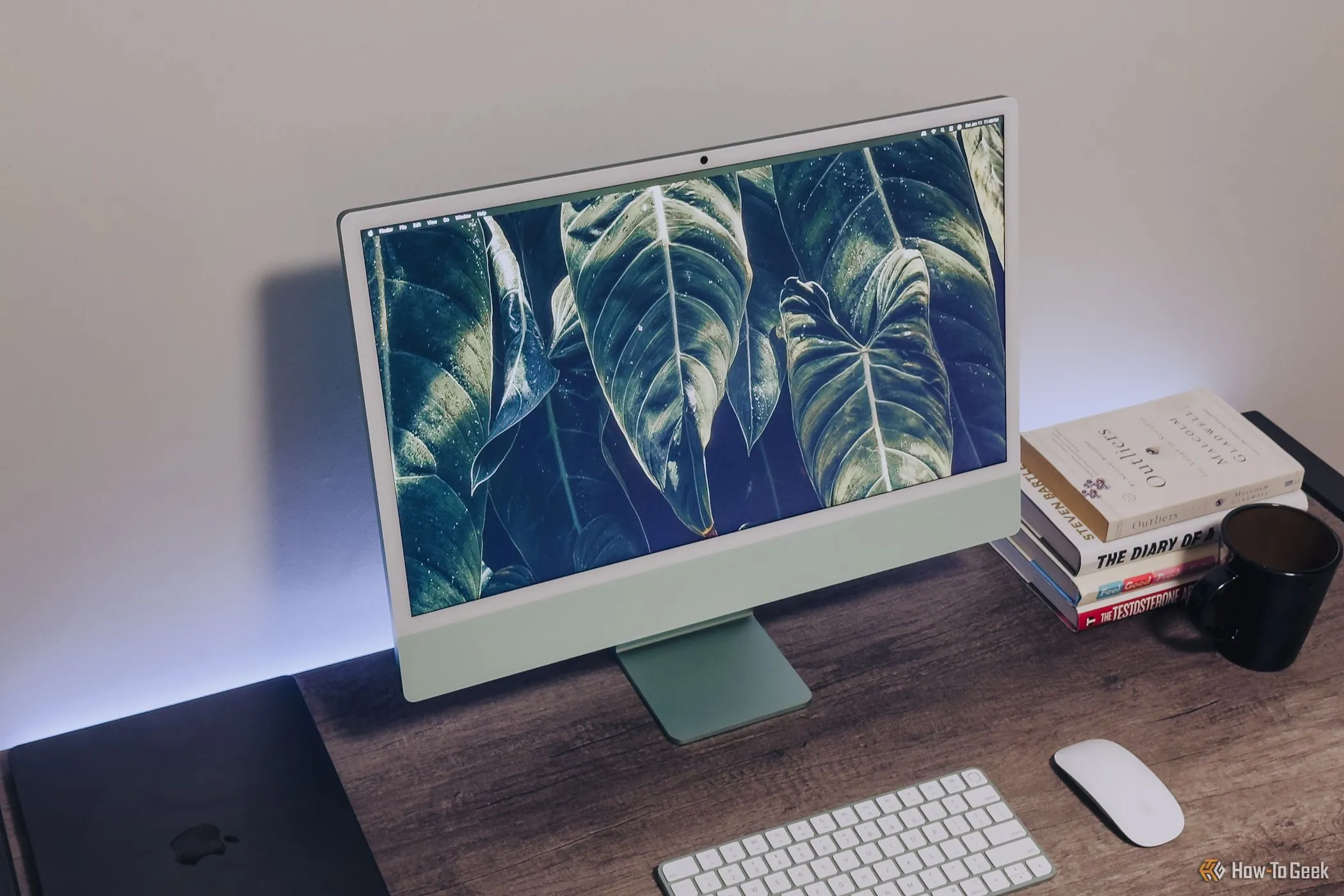 iMac M4 màu xanh đặt trên bàn gỗ, màn hình nhìn từ góc trên, thể hiện không gian làm việc cố định.