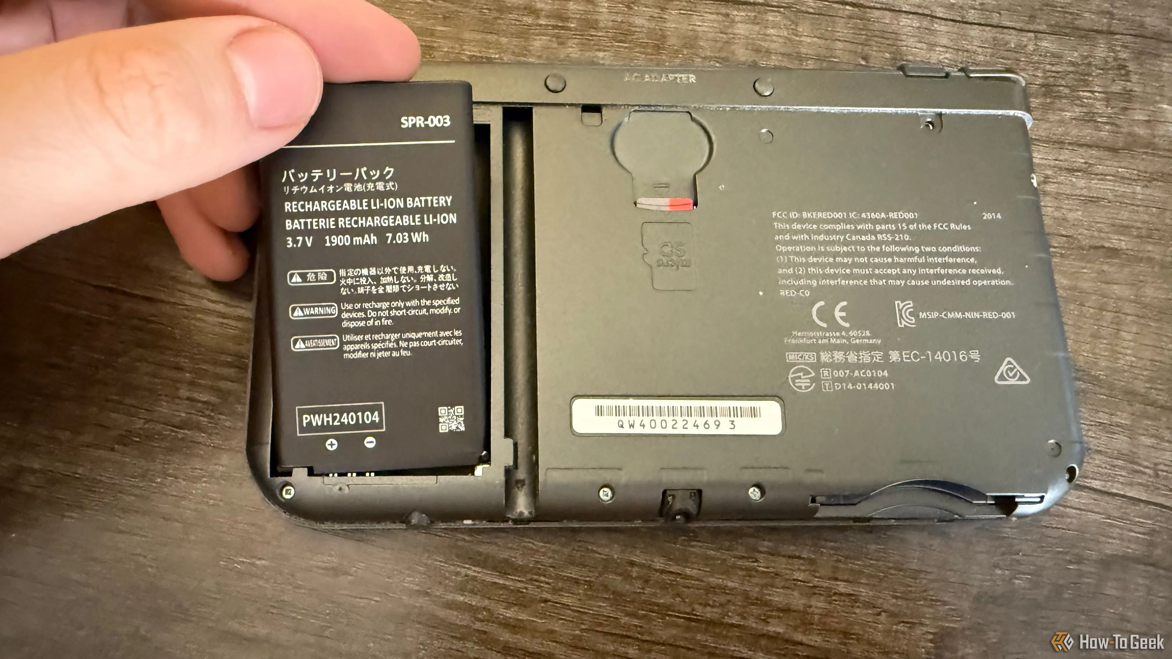 Một bàn tay đang đặt viên pin thay thế vào khe pin của New Nintendo 3DS XL