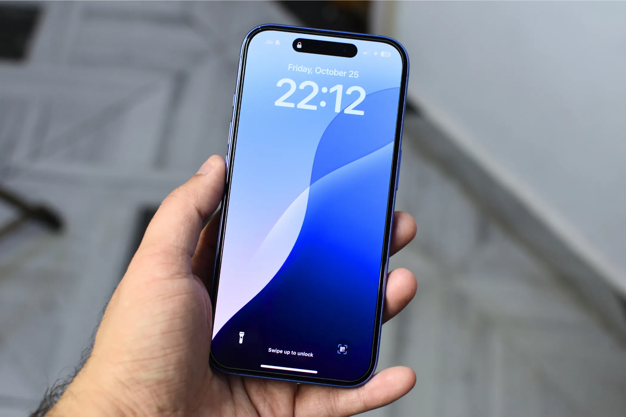 Một chiếc iPhone 16 màu xanh lam đang hiển thị màn hình khóa, được cầm trên tay người dùng.