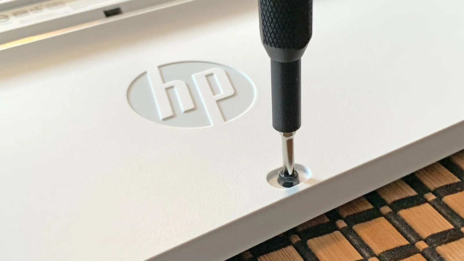 Một chiếc tua vít đang tháo ốc vít trên bàn phím của một máy tính HP, minh họa quá trình tháo lắp linh kiện PC.