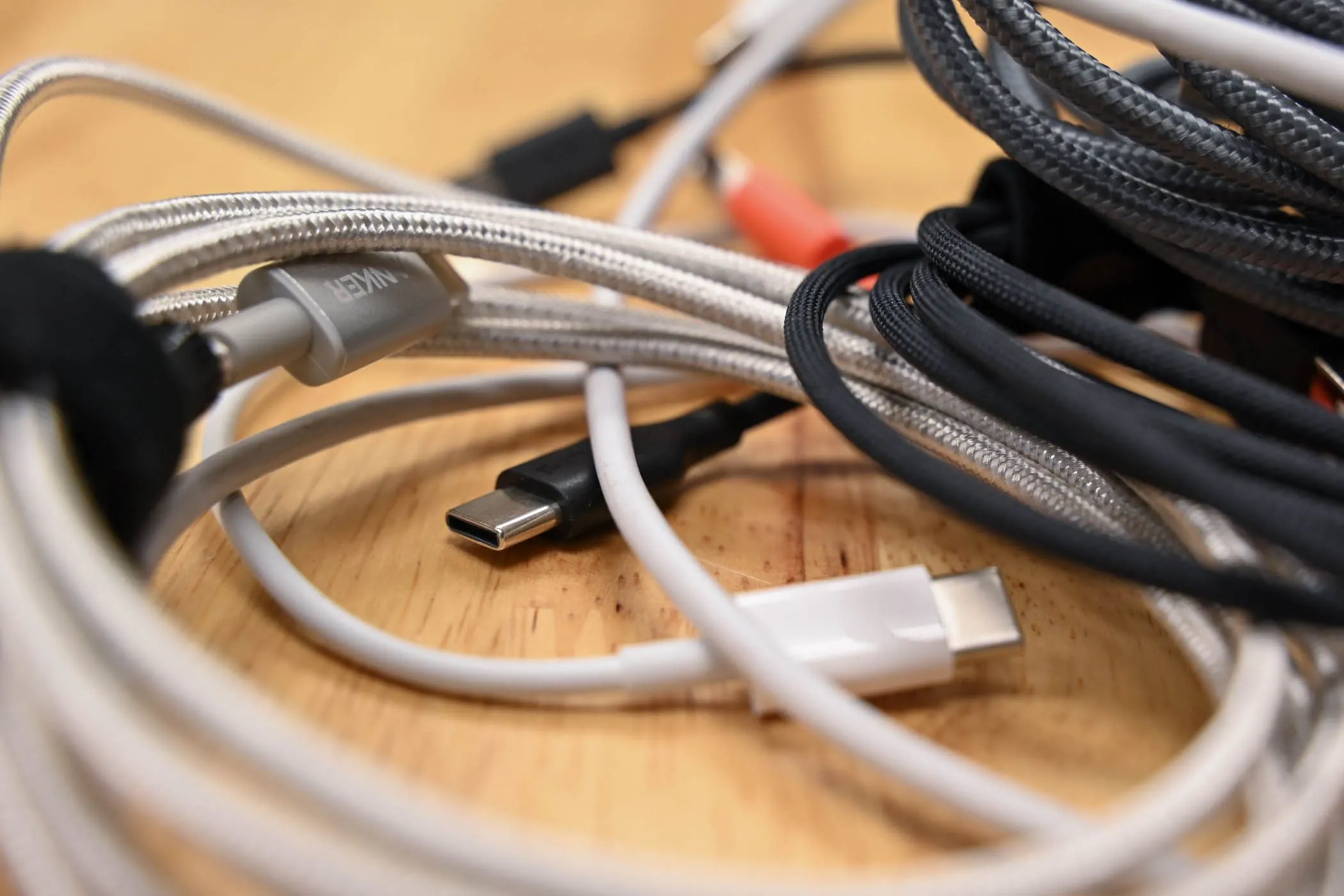 Một đống cáp USB-C đủ loại trên bề mặt gỗ, minh họa sự đa dạng của cáp USB-C