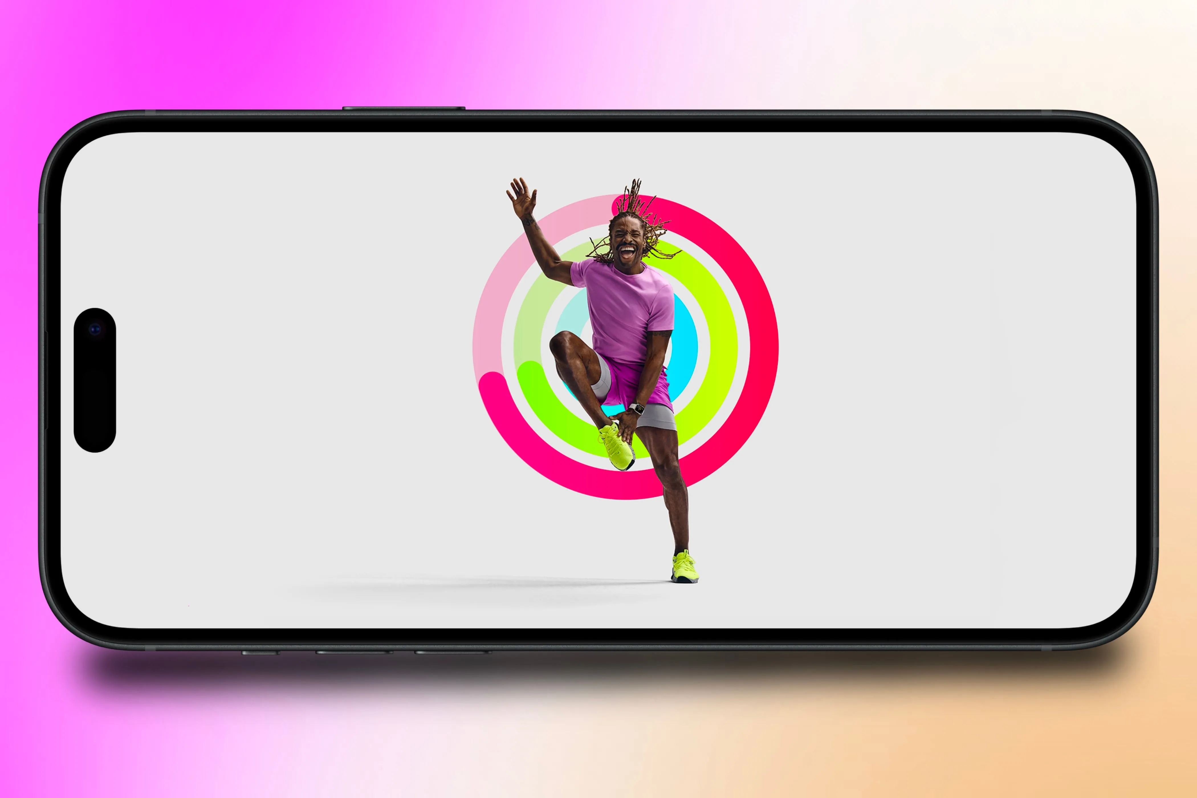 Một huấn luyện viên Apple Fitness+ đang tập luyện trước một bộ vòng Hoạt động (Activity Rings) hiển thị trên iPhone, trước một nền đầy màu sắc.