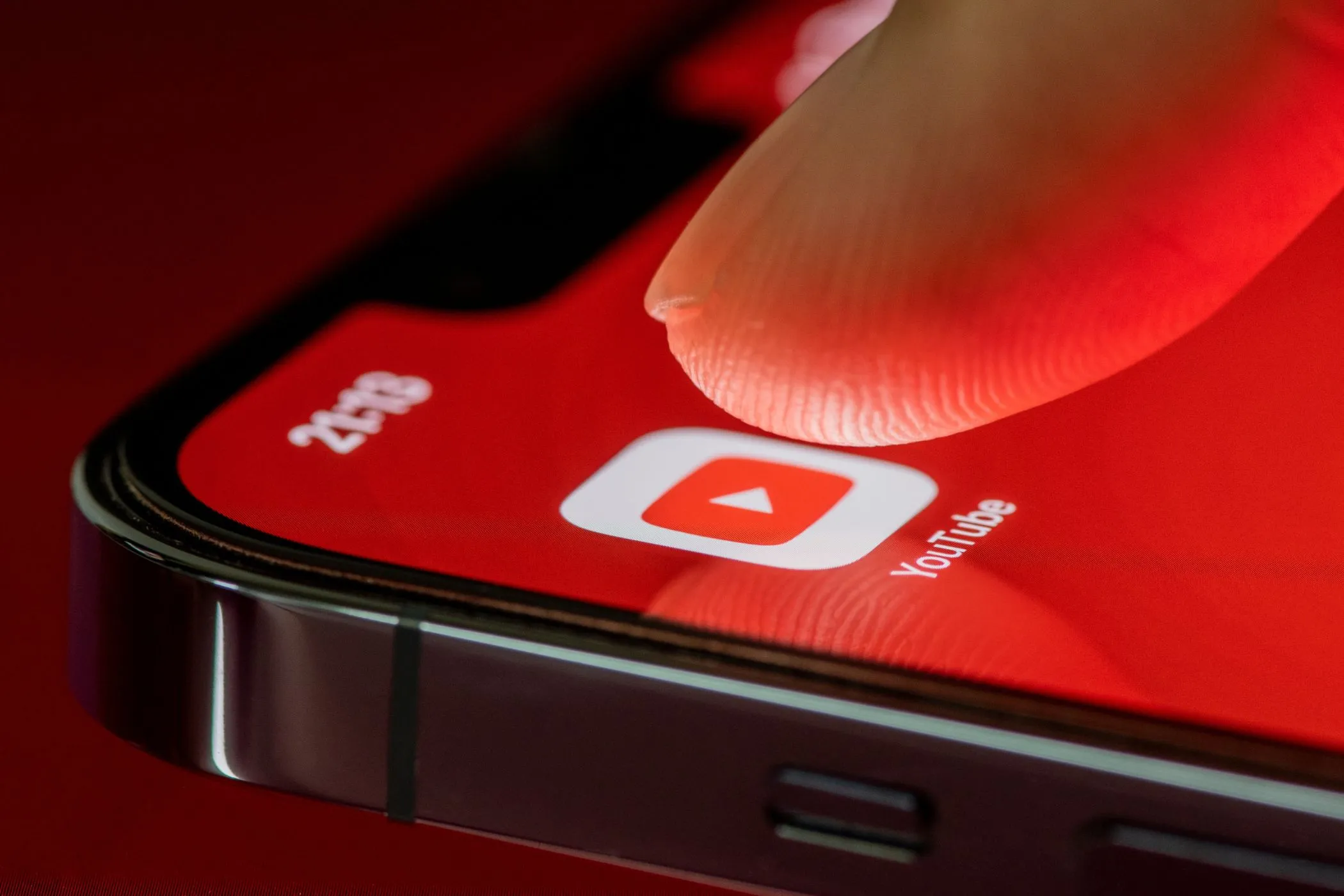 Một ngón tay đang chạm vào biểu tượng ứng dụng YouTube trên màn hình điện thoại iPhone.