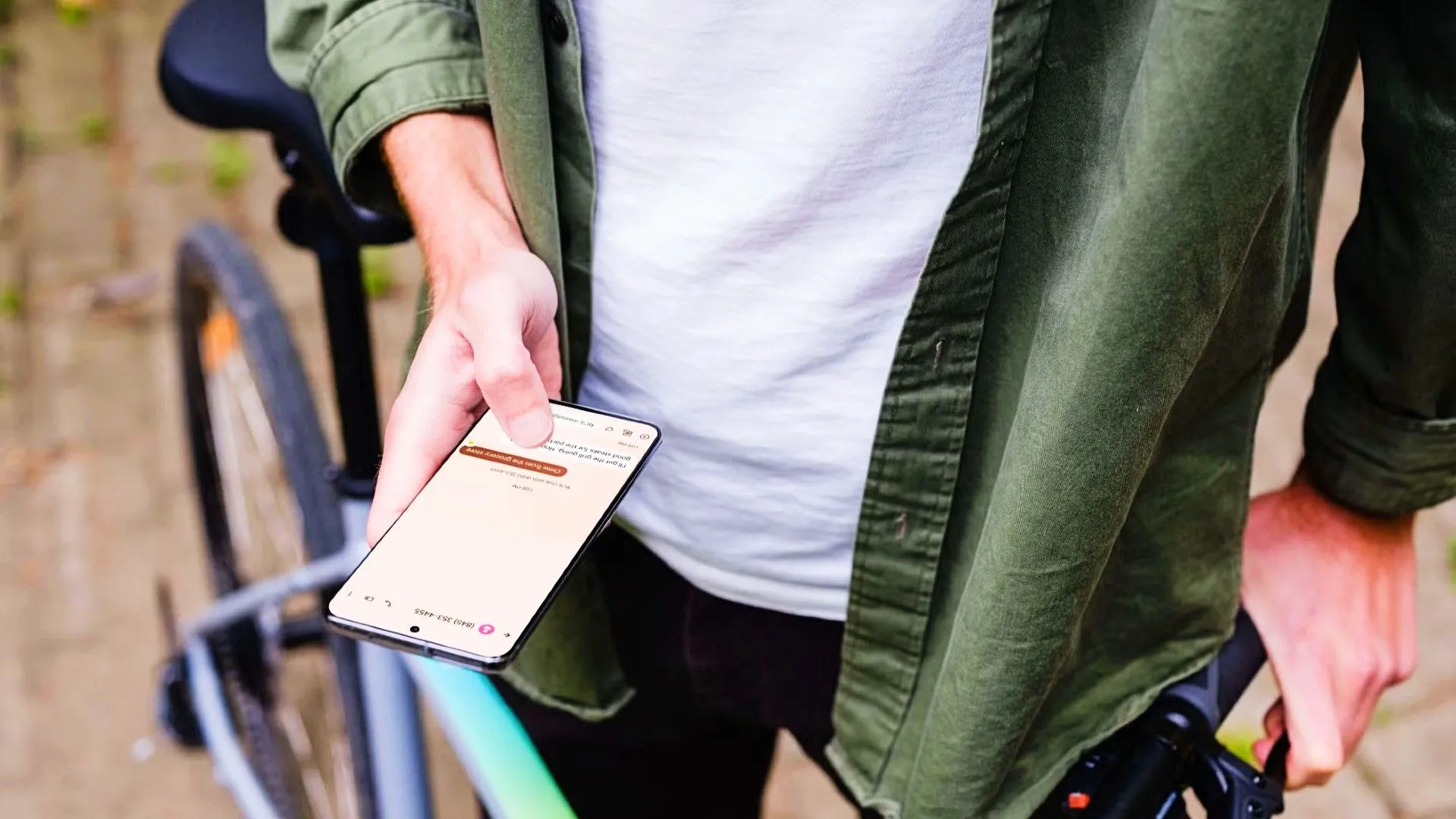 Một người đang cầm điện thoại Android bên cạnh xe đạp, màn hình hiển thị cuộc trò chuyện văn bản, minh họa tính năng Quick Tap