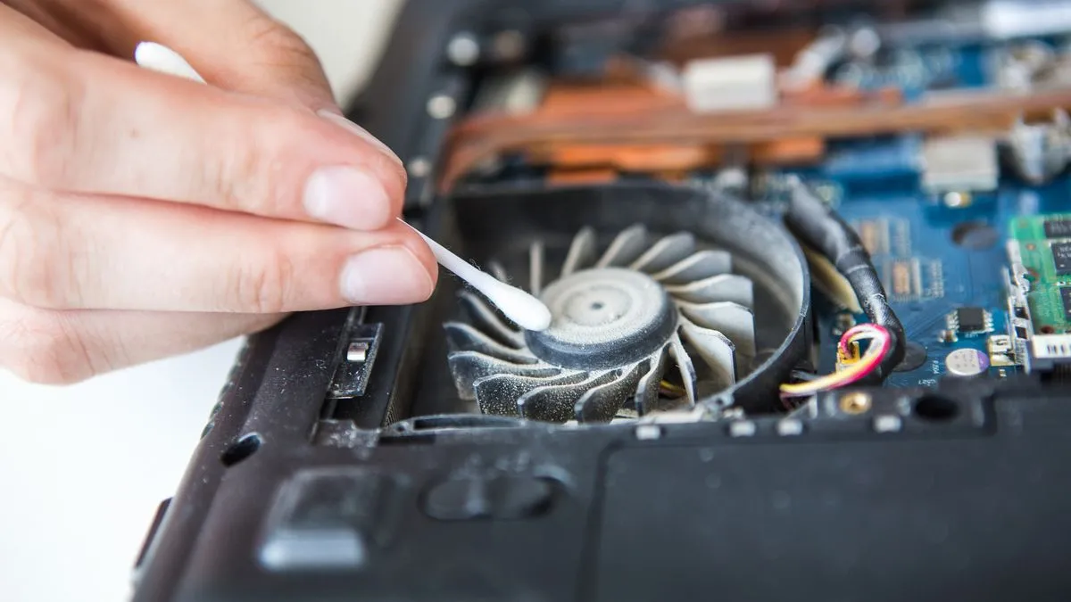 Một người đang làm sạch bụi bẩn từ bên trong laptop bằng tăm bông, tập trung vào các khu vực nhỏ và khó tiếp cận.