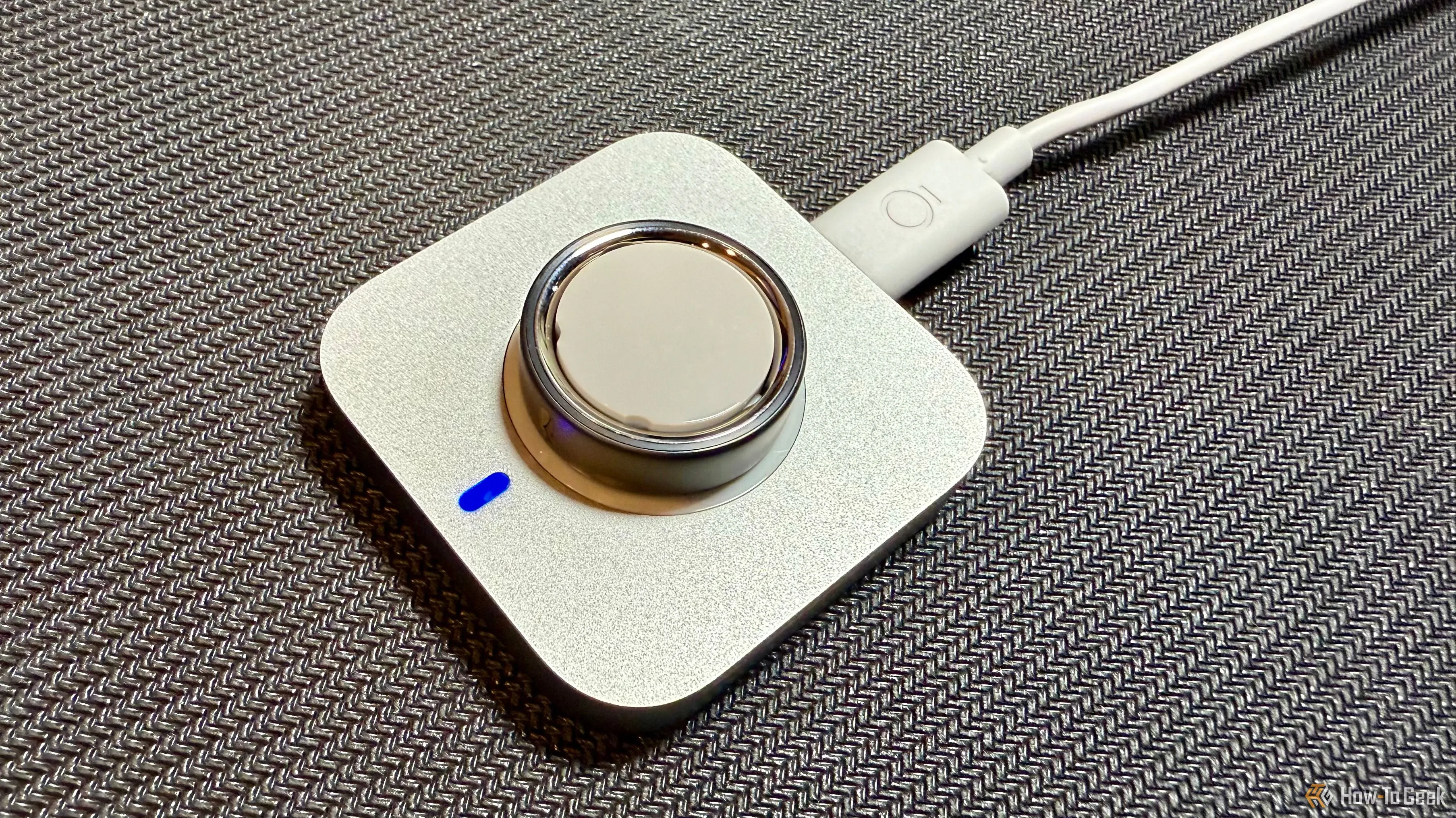Nhẫn Oura Ring 4 đang được sạc trên đế sạc chuyên dụng, thể hiện đèn báo pin.