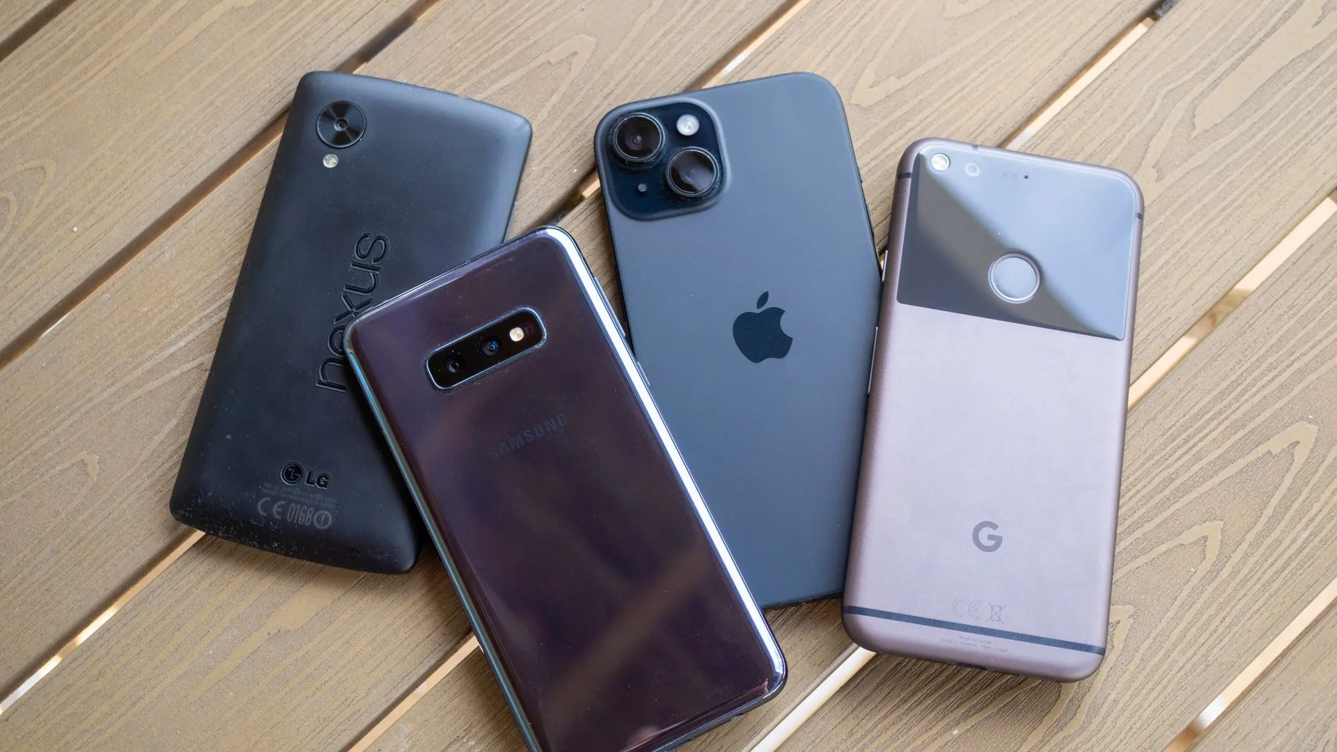 Nhiều mẫu điện thoại cũ từ các thương hiệu Nexus 5, Galaxy S10e, iPhone 15 và Google Pixel đặt trên bàn, tượng trưng cho những chiếc điện thoại cũ có thể được tái sử dụng hoặc tặng lại.