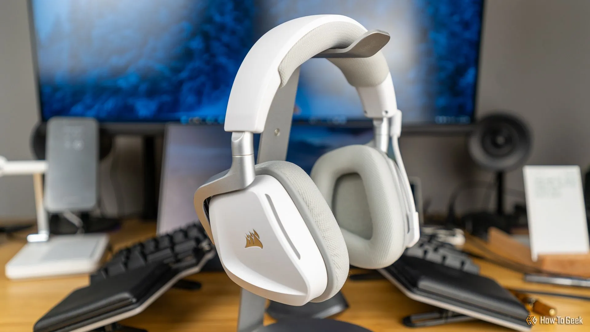 Tai nghe gaming Corsair Void Wireless V2 màu trắng đặt trên giá đỡ, bố cục bàn làm việc gọn gàng