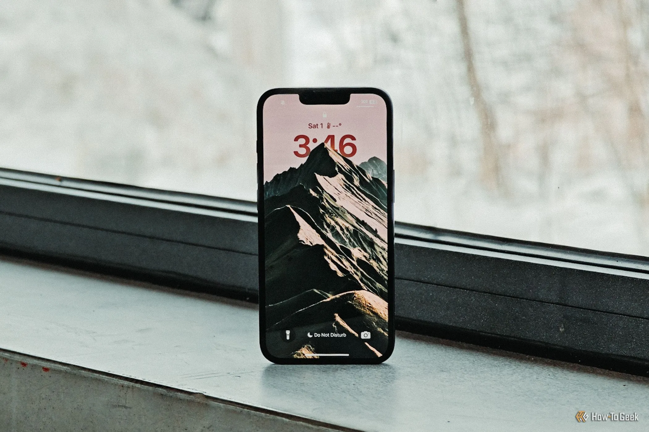 Màn hình khóa iPhone 16e đặt trước cửa sổ, phản ánh rõ nét thiết kế &quot;tai thỏ&quot; và tần số quét 60Hz cơ bản của màn hình OLED