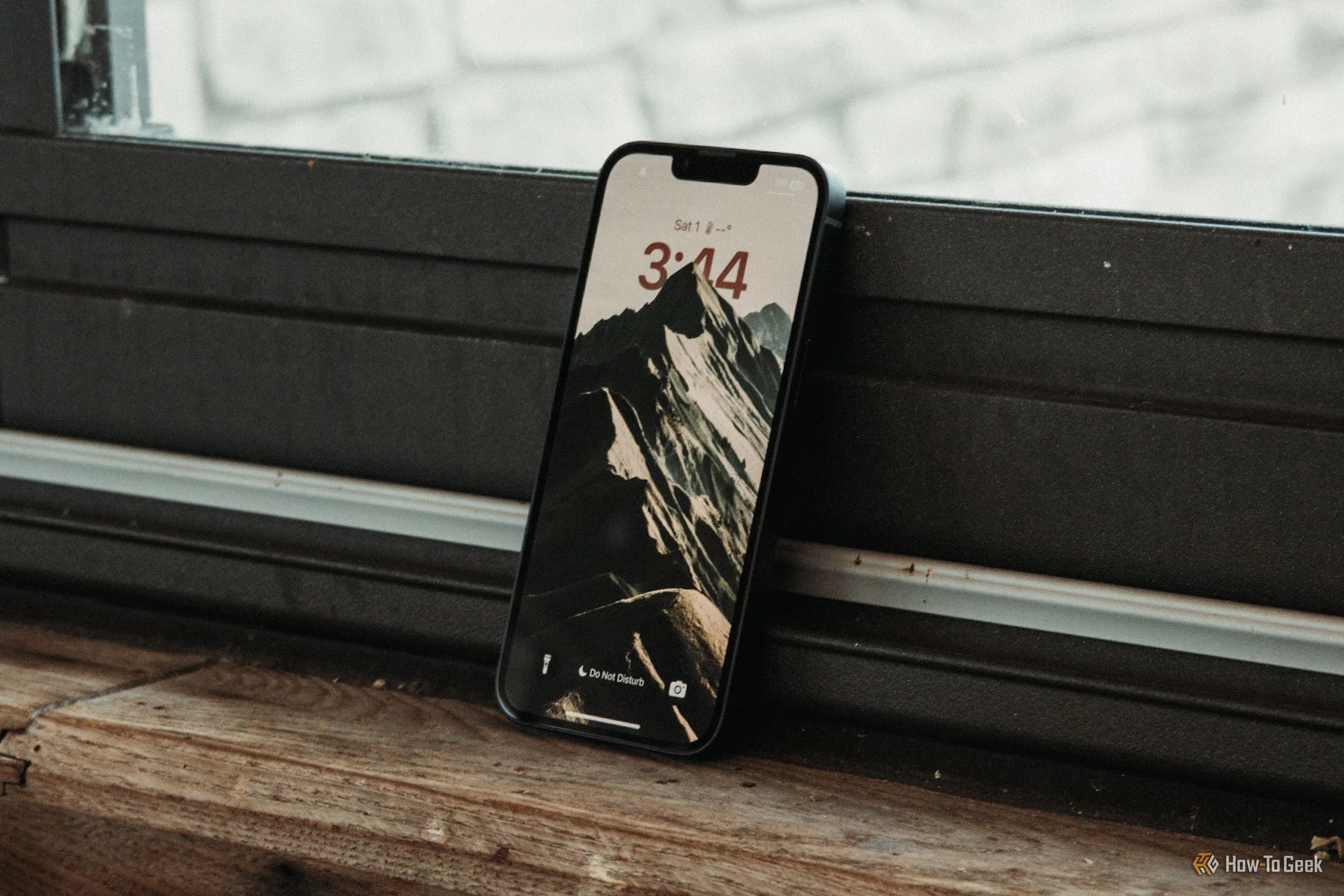 Màn hình khóa iPhone 16e hiển thị giao diện iOS với &quot;tai thỏ&quot; quen thuộc, đặt nghiêng cạnh cửa sổ, thể hiện đặc điểm thiết kế màn hình