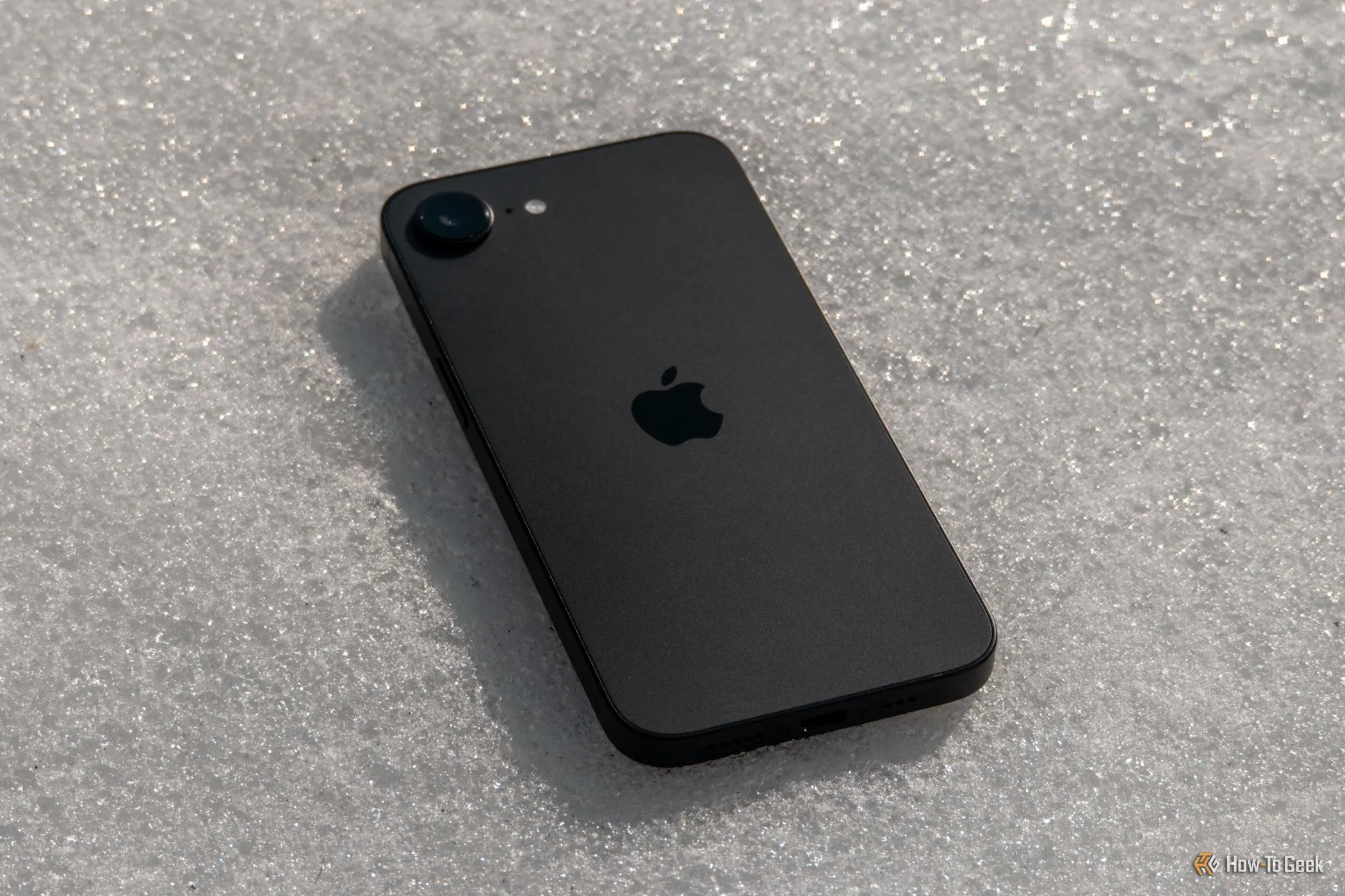 Mặt lưng iPhone 16e màu trắng đặt úp trên nền tuyết, làm nổi bật cụm camera đơn gọn gàng và độc đáo của mẫu smartphone này