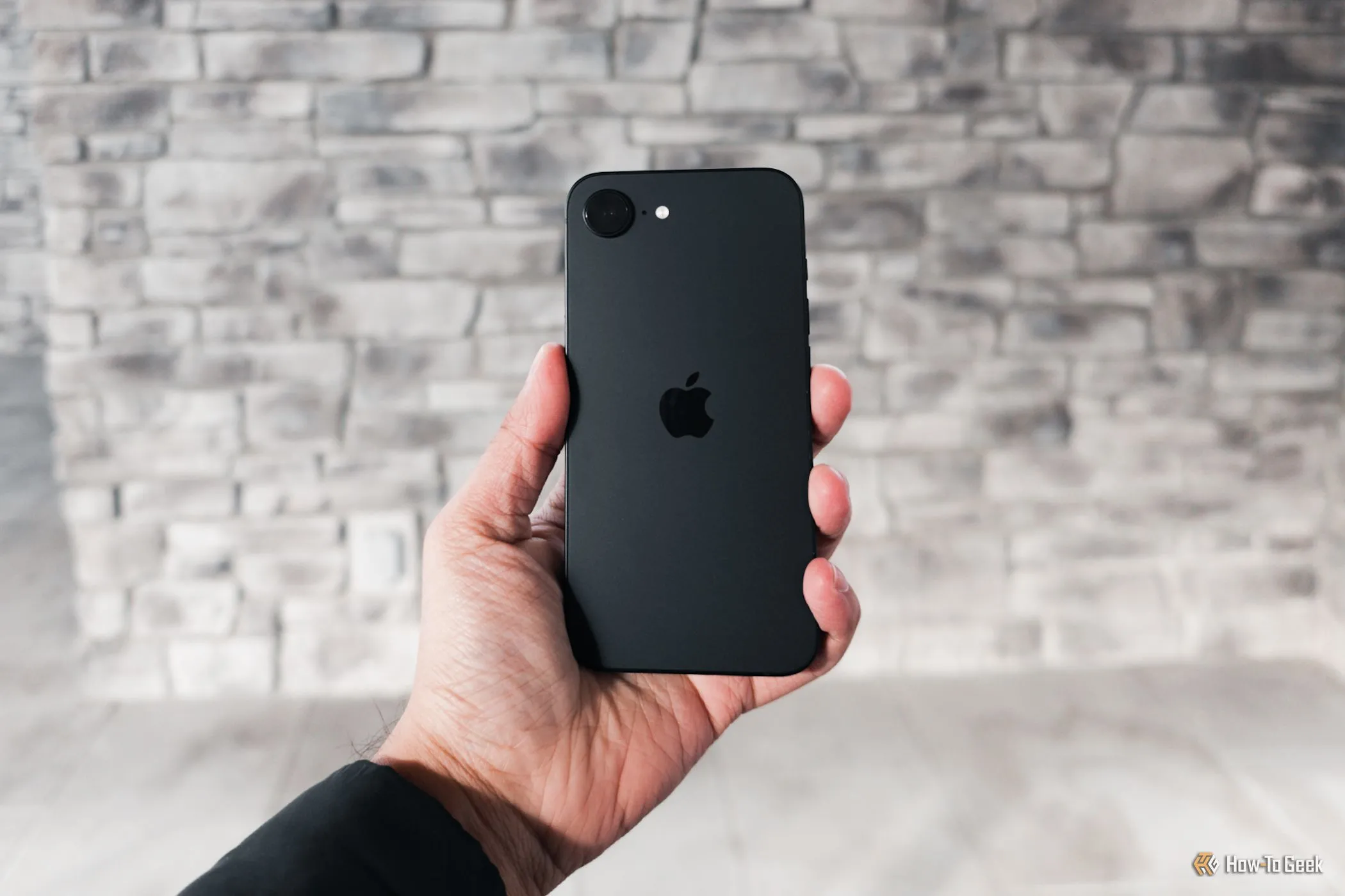 Người dùng cầm iPhone 16e trên tay với hình nền màu xám, trải nghiệm thời lượng pin ấn tượng cả ngày dài nhờ tối ưu chip A18 và modem C1