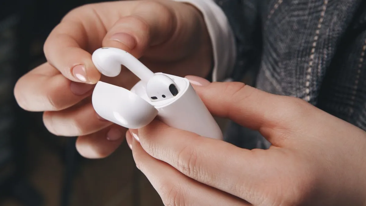 Người đang lấy tai nghe AirPods ra khỏi hộp sạc, gợi lên vấn đề vệ sinh và sự tích tụ bụi bẩn khi sử dụng hàng ngày.